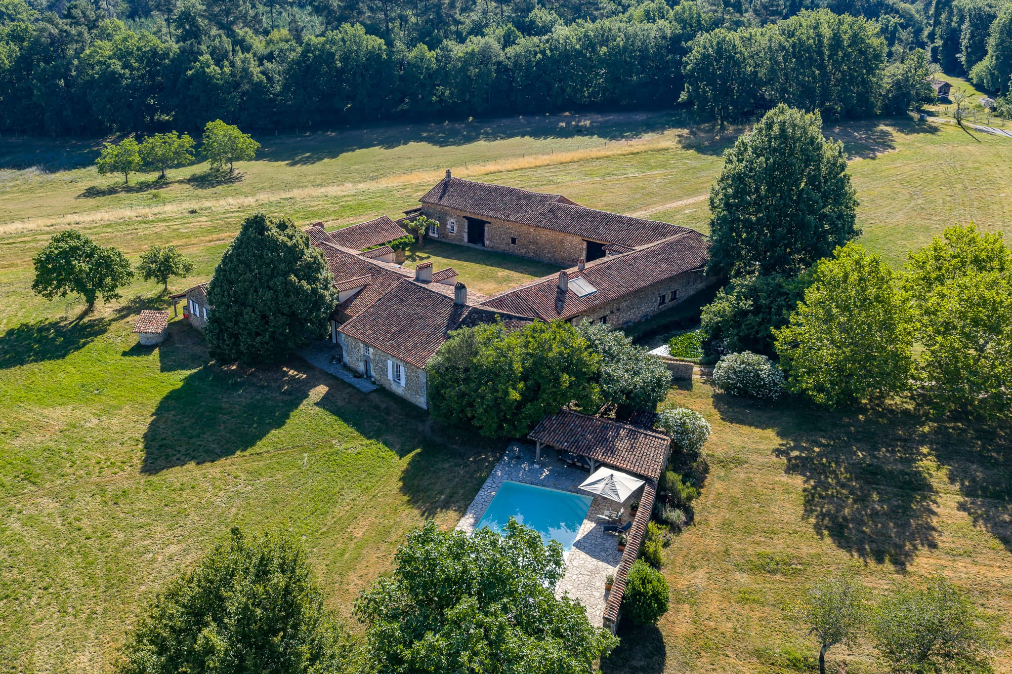 Aerial view of Le Clos de Moncouche: three Périgord stone wings around a courtyard, a pool, and surrounding meadows.