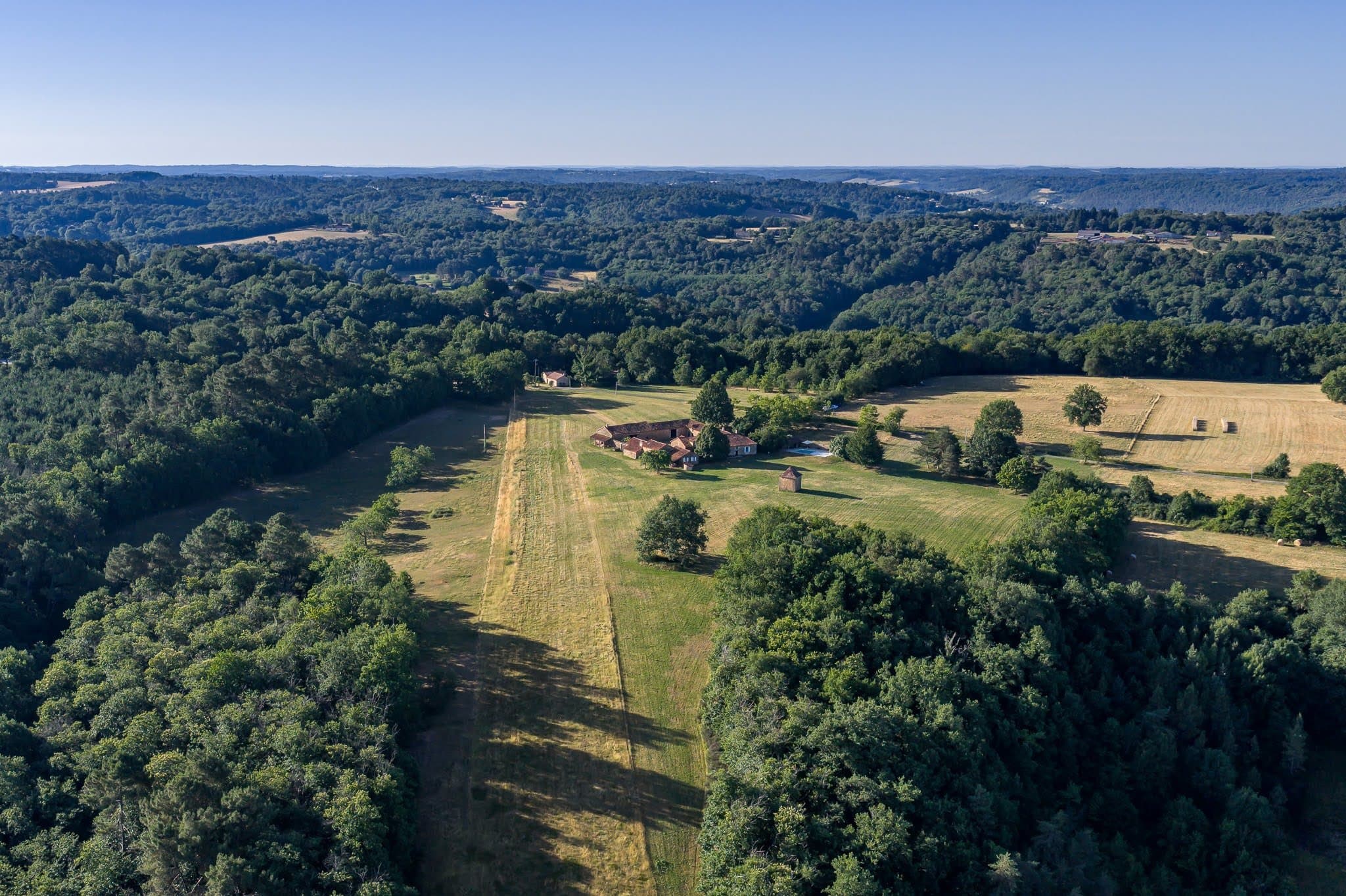 Aerial view of the estate: the courtyard, the pool and the pigeonnier amid meadows and woodland.
